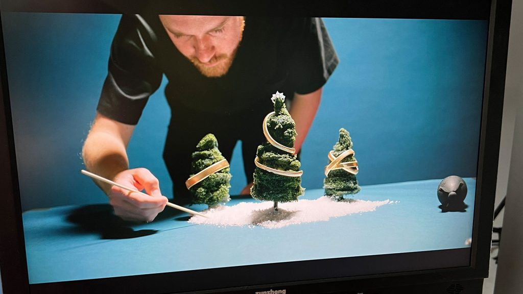 A man adjusting three model Christmas trees with a stick on a blue set